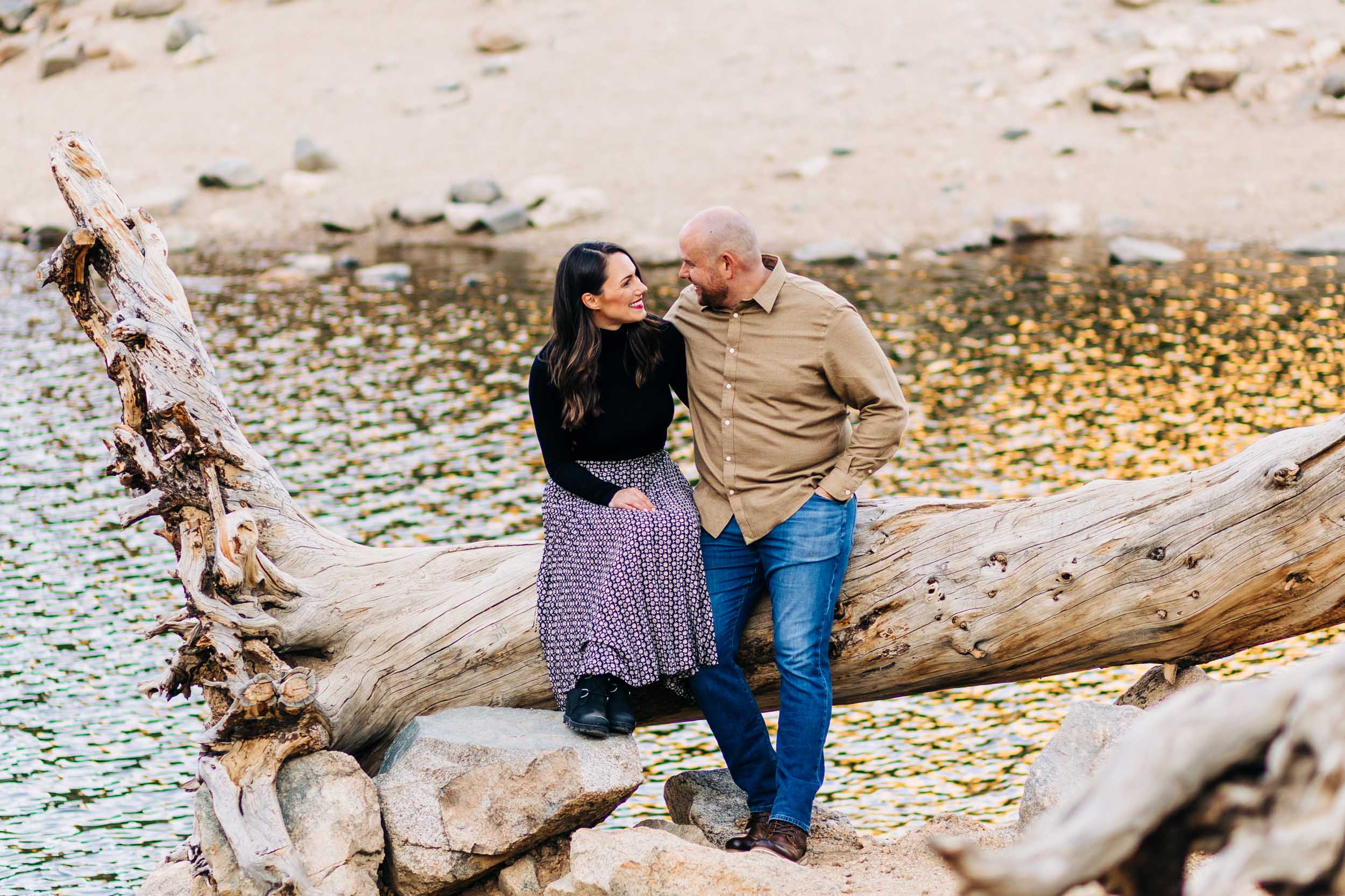 couple look at each other while sitting on a log at st Mary's glacier