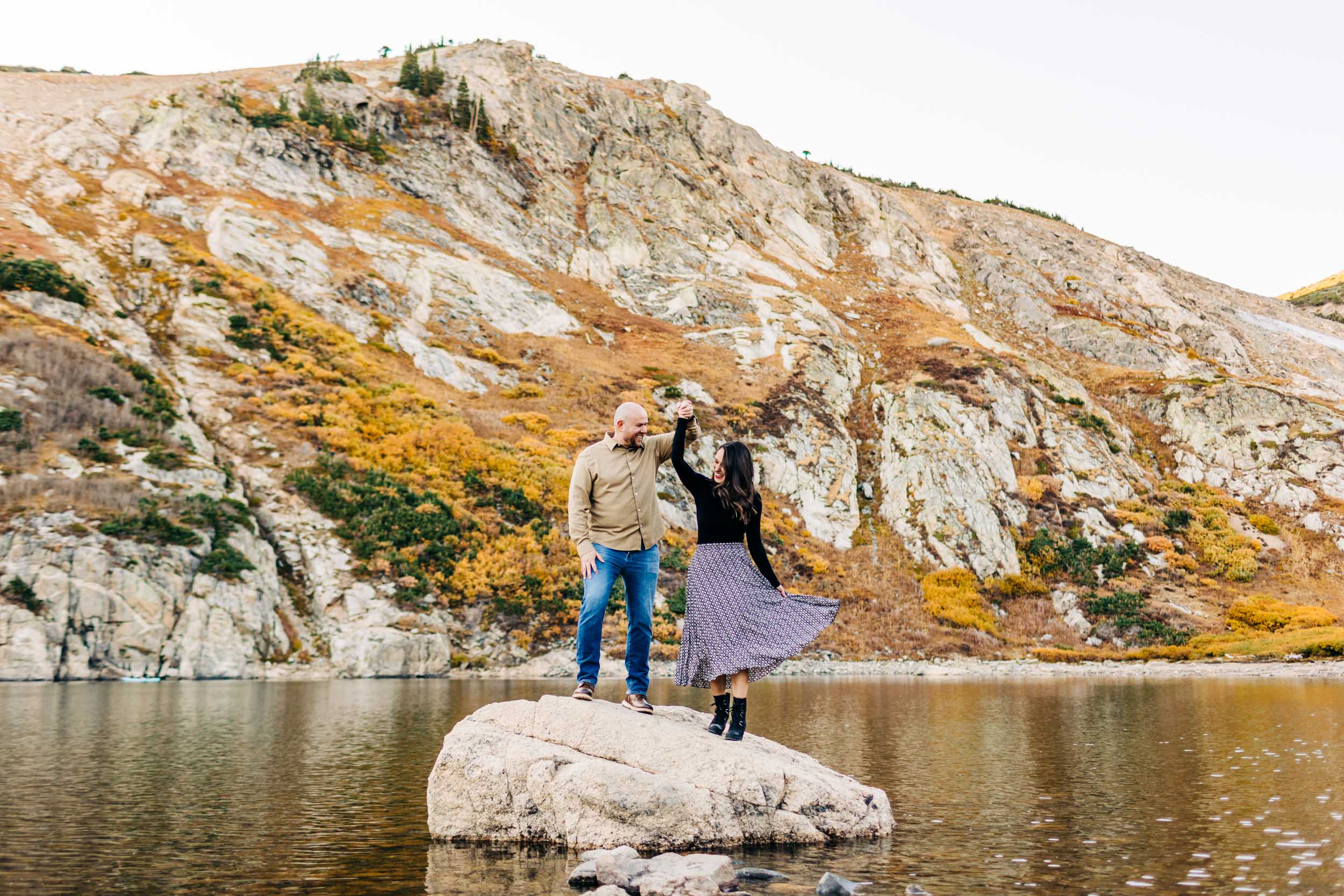 fall engagement photo at st Mary's glacier of couple dancing on the rock
