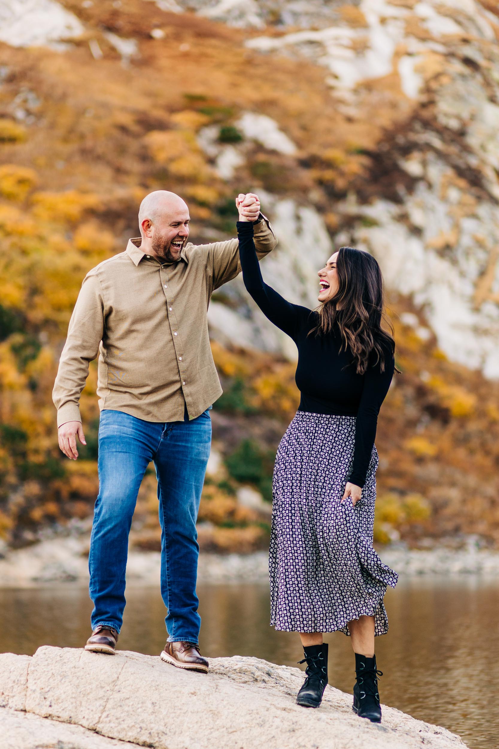 fall engagement photo at st Mary's glacier of couple dancing on the rock