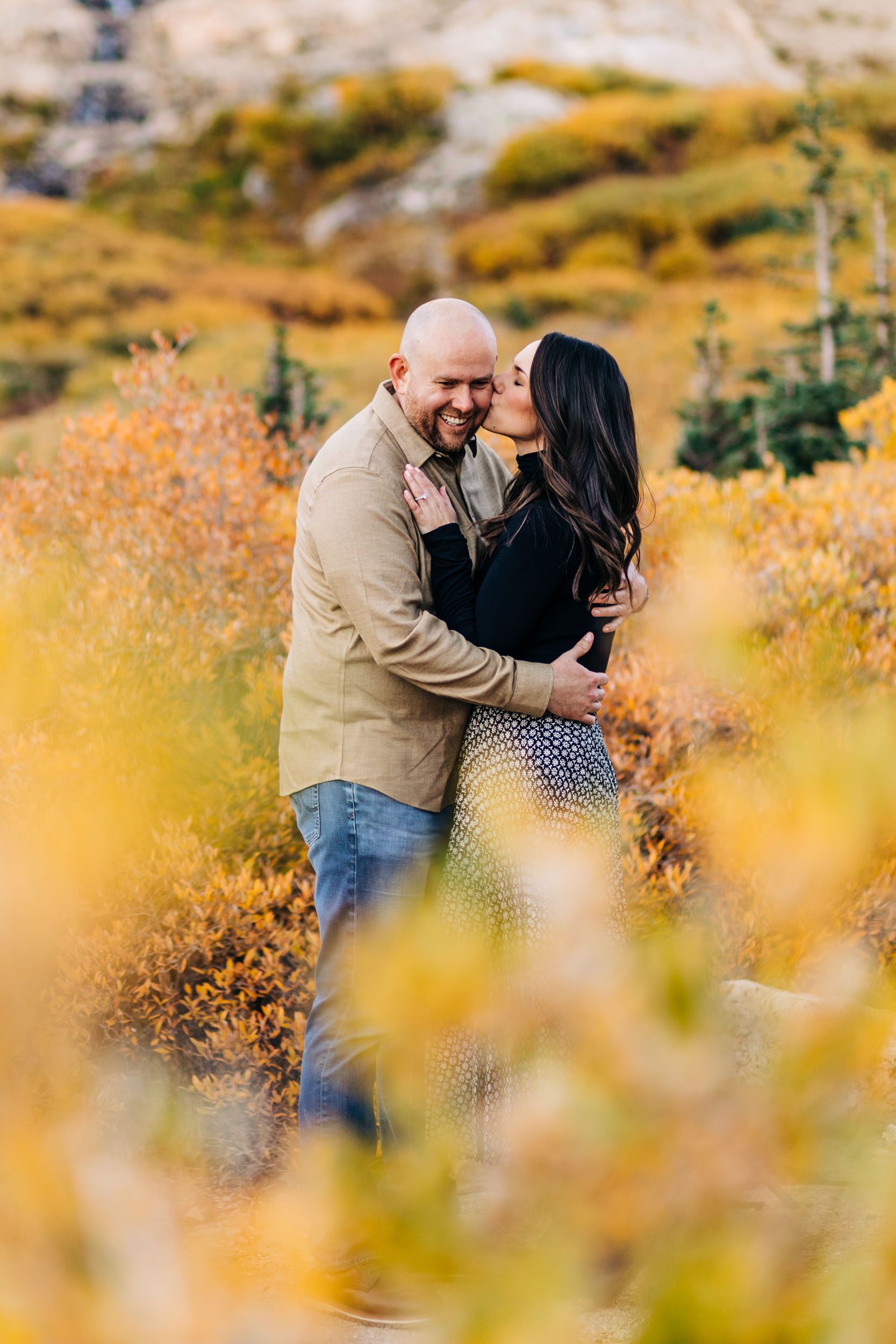 classic fall engagement photo where woman is kissing man's cheek