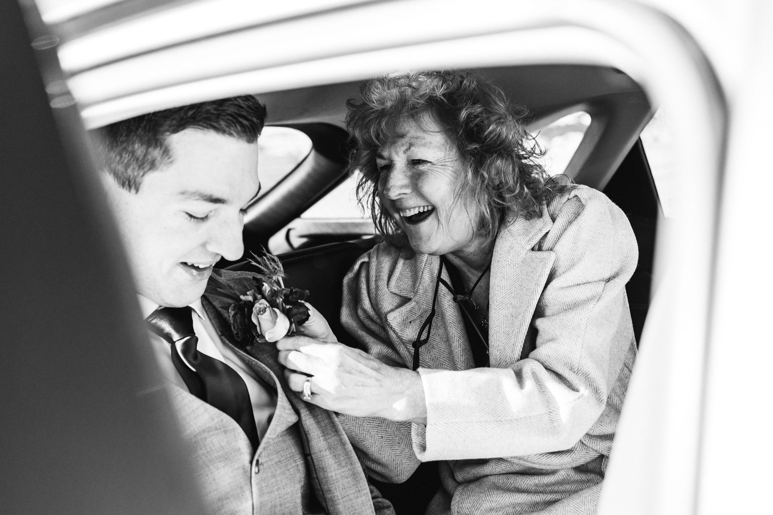 mother of the groom putting boutonniere on in the car