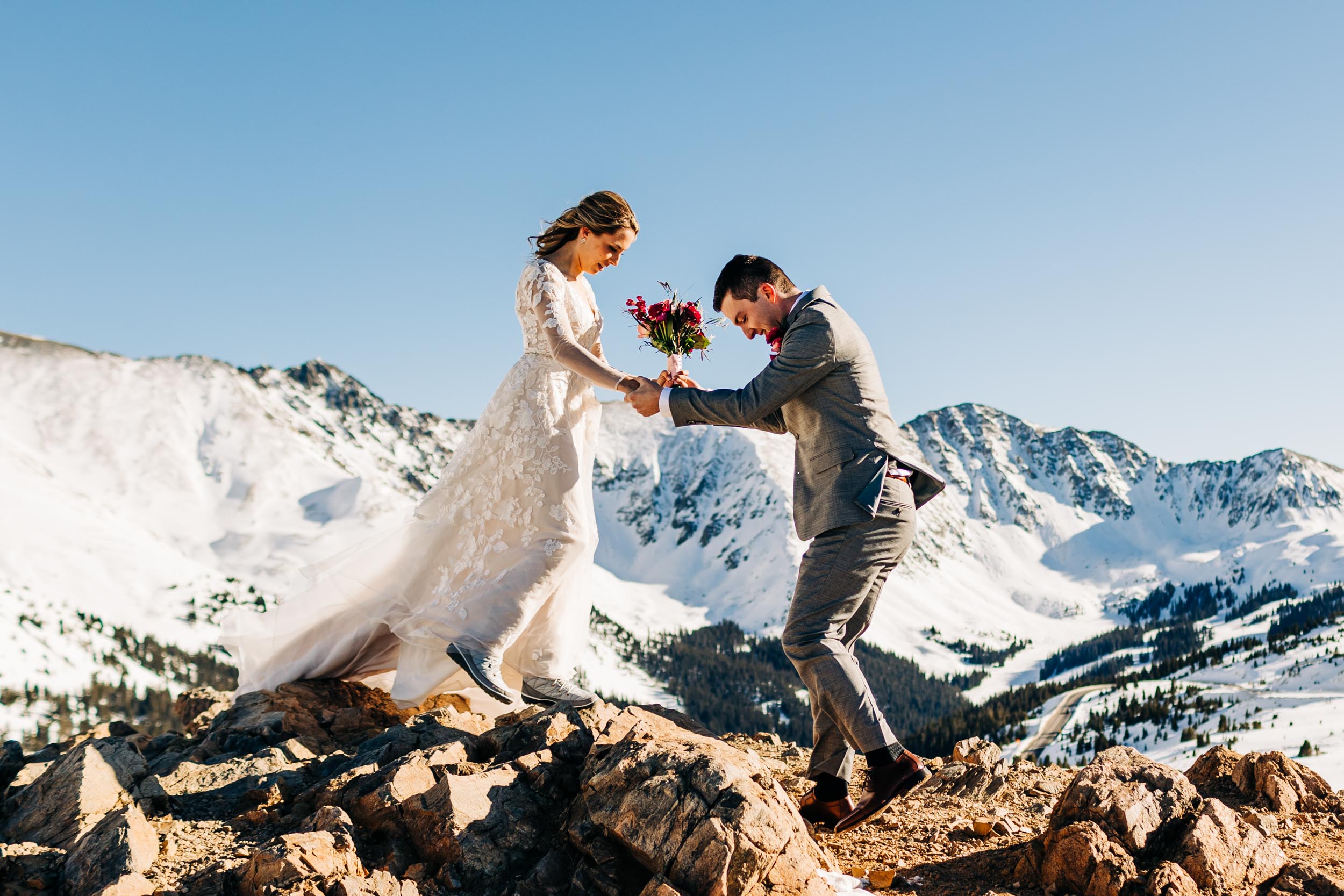 groom helping bride down off of a rock at loveland pass